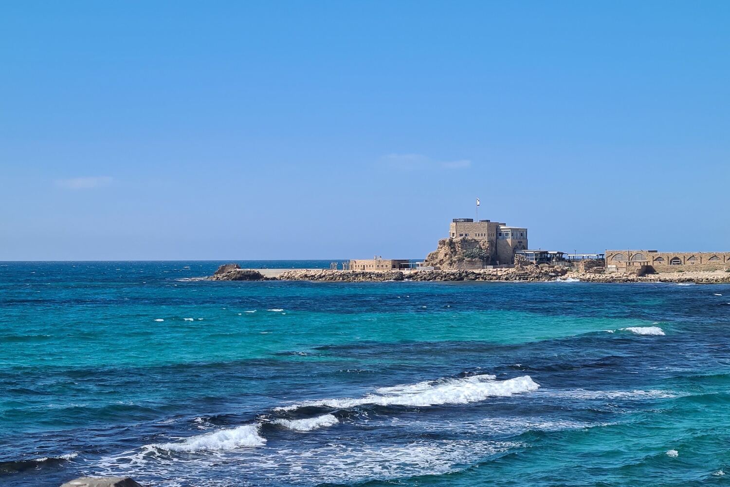 The ruined harbour fortress at Caesarea on its stone mole, turquoise water breaking around it