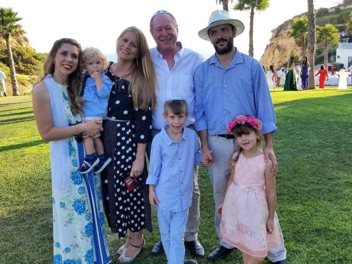 Daniela com a família — três gerações juntas num gramado acima do mar, com palmeiras ao fundo