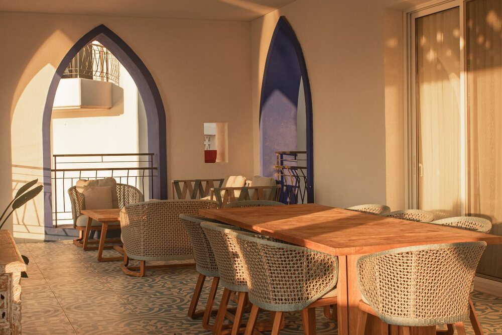 Uma sala de jantar mobiliada com cadeiras de fibra e mesa de madeira, vista através de arcos altos num interior claro